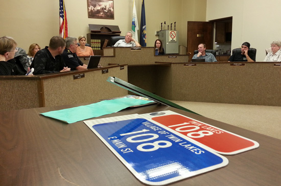 Twin Lakes village officials discuss 911 address signs Monday, with two examples of signs in the foreground.