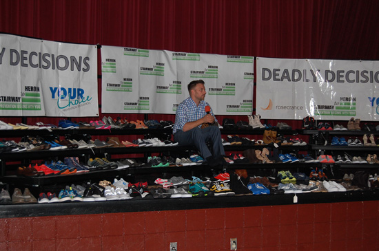 Tyler Lyberg of Your Choice Preventative Education sits among 144 pairs of empty shoes representing the deaths from heroin overdoses in Kenosha County 2013-2015.